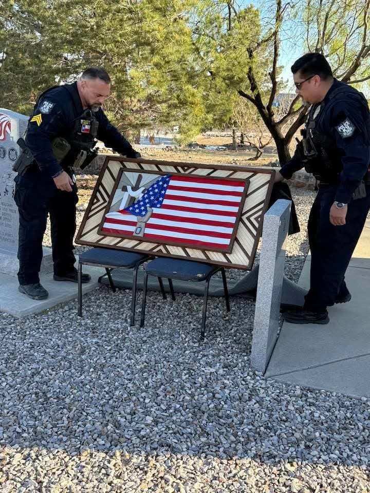 Two police K9 officers placing a memorial shadow box at a fallen handler's gravesite