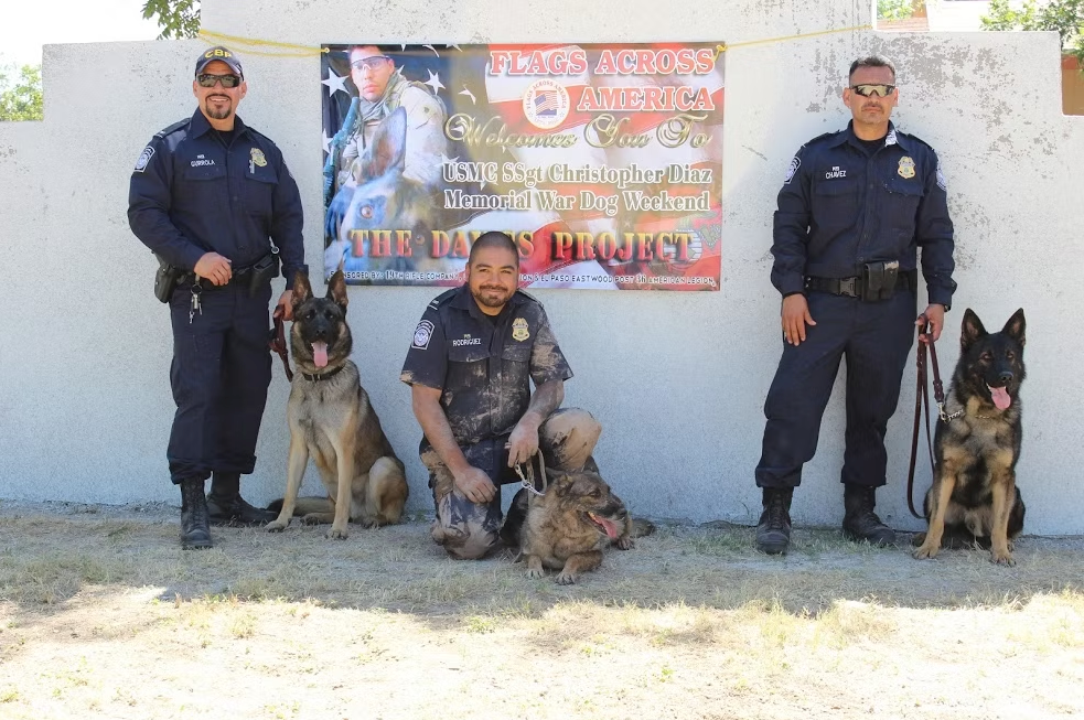 A police K9 officer kneeling with his working dog beside a memorial banner