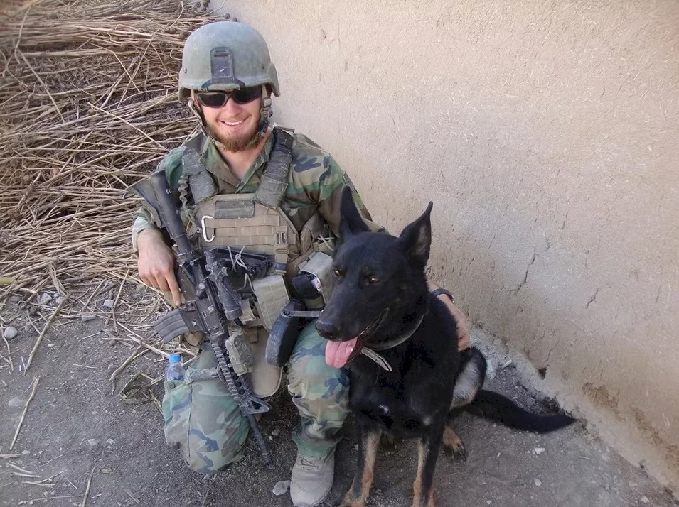 A military K9 handler in gear with a working dog