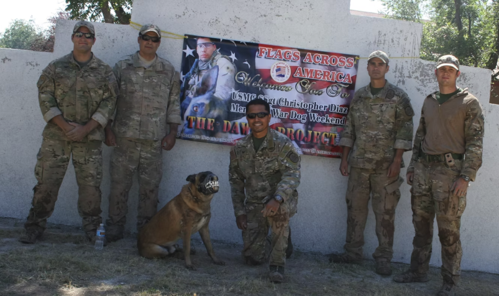 Soldiers posing with a working dog in front of a tribute banner